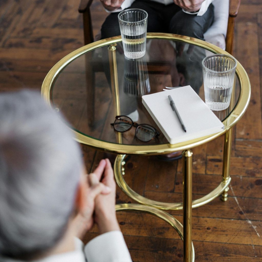 Two adults discussing mental health in a counseling session across a glass table indoors.