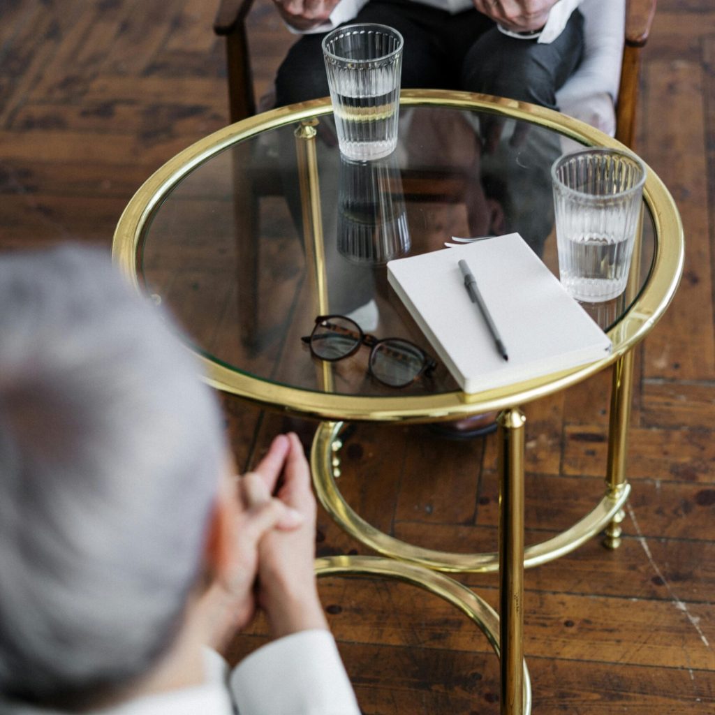 pexels-photo-4098369-4098369 Two adults discussing mental health in a counseling session across a glass table indoors.